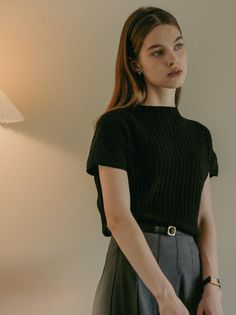 Woman with long hair and a headband wearing a black top and grey skirt indoors