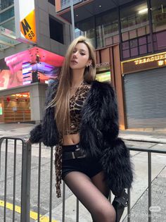Woman in a black fur coat and leopard print top posing on a city street at night