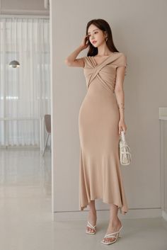 Woman in a beige dress and white high heels holding a handbag indoors