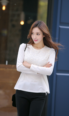 Woman with long brown hair wearing a white lace top and black pants outdoors