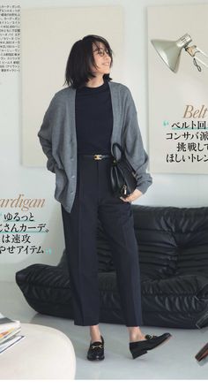 Woman in a gray cardigan and black pants holding a handbag indoors
