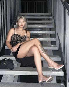 Woman with blonde hair and tattoos sitting on metal stairs at night