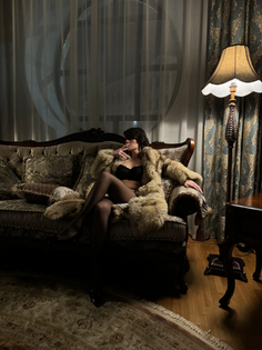 Woman in a fur coat and lingerie on an ornate sofa in a dimly lit room