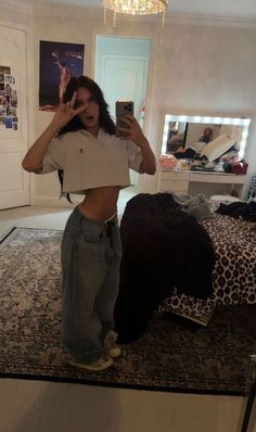 Woman in a crop top and baggy jeans taking a mirror selfie in a bedroom