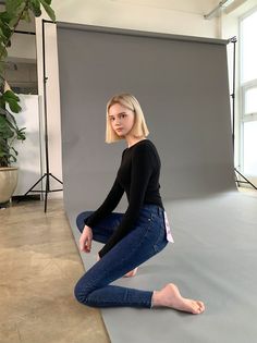 Woman with blonde bob hair in a black top and blue jeans posing in a studio
