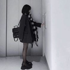 Person in a black coat and plaid scarf pressing an elevator button