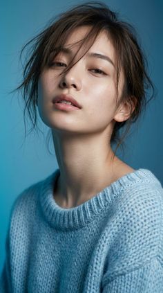 Woman with messy brown hair wearing a light blue sweater against a blue background