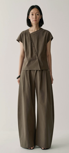Woman in a dark olive asymmetrical top and wide leg pants in a studio