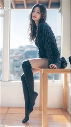 Woman in a black dress and thigh-high socks sitting on a table by a window