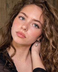 Woman with curly hair and green eyes wearing pearl earrings
