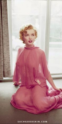 Woman with blonde hair in a sheer pink dress kneeling by a window