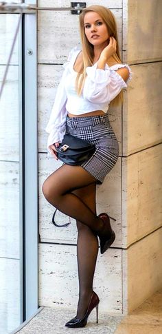 Woman in a white crop top and plaid skirt posing indoors