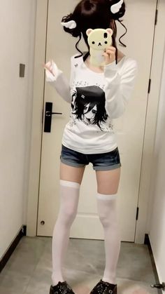 Person in denim shorts and a long sleeve shirt with anime print, holding a phone