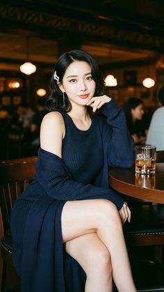 Woman in a dark blue dress and cardigan sitting at a bar with a drink