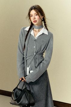 Woman with braided hair wearing a gray cardigan and white shirt, holding a black handbag