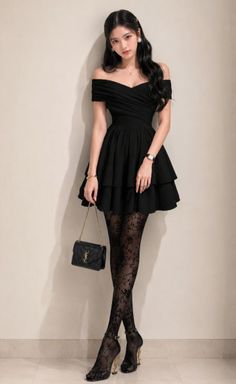 Woman in a black off-shoulder dress and lace tights holding a small bag