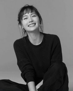 Woman with bangs and hoop earrings smiling in a black and white studio shot