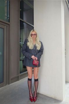 Woman with blonde hair wearing an oversized blazer, red heels, and knee-high socks