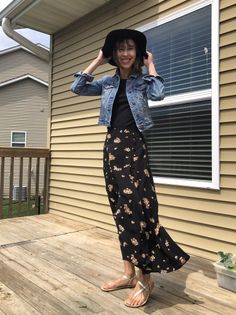 Woman in a denim jacket and floral skirt posing on a wooden deck