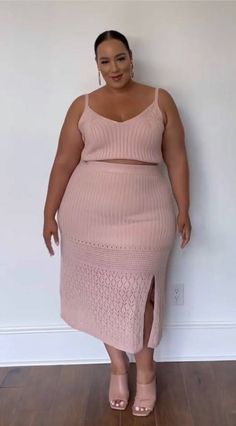 Woman with a curvy body wearing a pink knitted crop top and midi skirt indoors