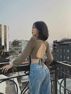 Woman with short hair in a crop top and jeans on a rooftop overlooking a cityscape