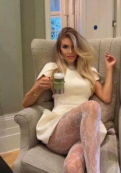Woman with blonde hair in a white dress and lace tights holding a drink