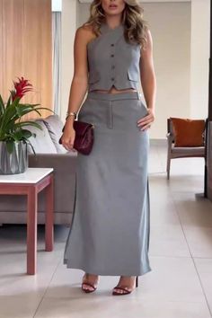 Woman in a gray sleeveless top and long skirt holding a red clutch