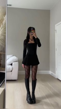 Woman in a black dress and patterned tights taking a mirror selfie indoors
