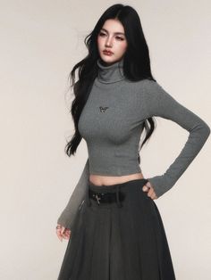 Woman with long black hair in a grey cropped turtleneck and dark skirt