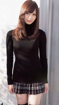 Woman with long brown hair wearing a black turtleneck and plaid skirt indoors