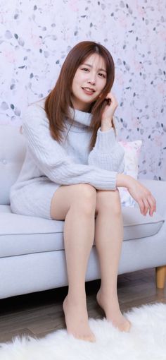 Woman with long hair wearing a light sweater dress, sitting on a sofa indoors