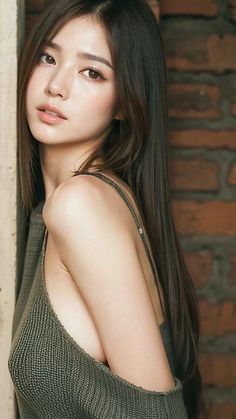 Woman with long dark hair and exposed shoulder against a brick wall