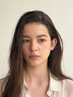 Woman with long brown hair wearing a white shirt, looking directly at the camera