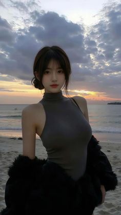 Woman in a turtleneck top and black jacket on a beach at sunset