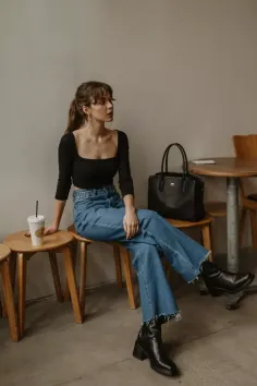 Woman in a black crop top and blue jeans sitting indoors