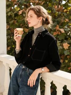 Woman in a black shirt and jeans holding a coffee cup outdoors