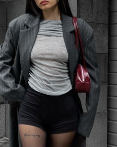 Person in a pinstripe blazer, grey top, and black shorts with a red handbag