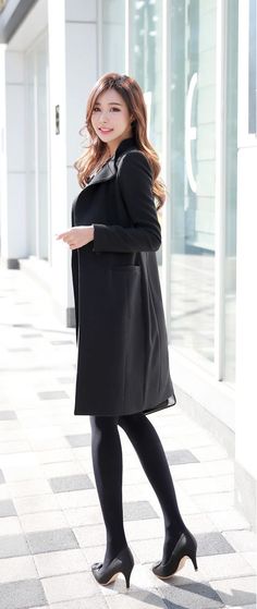 Woman in a black coat and tights standing outdoors