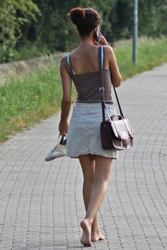 Woman walking barefoot on a paved path, holding shoes and talking on the phone