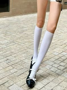 Person wearing white knee socks and black shoes with white laces on paved ground