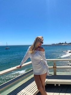 Woman in a white cover-up and bikini on a pier overlooking the ocean