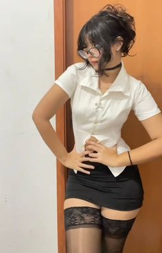 Woman in a white shirt, black mini skirt, and thigh high stockings posing indoors