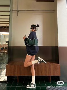 Person in an oversized sweatshirt, shorts, and sneakers posing indoors