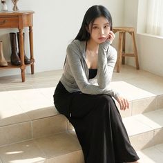 Woman with long black hair sitting indoors in a gray hoodie and black skirt