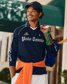 Man in a navy blue tennis shirt and cap, with an orange sweater tied around his waist