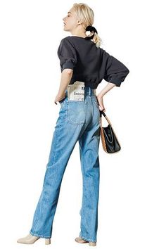 Woman with blonde hair in a cropped top and blue jeans, holding a handbag