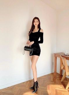 Woman in a black mini dress and high heels holding a small handbag indoors