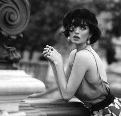 Woman with short hair and earrings leaning on a stone railing in black and white