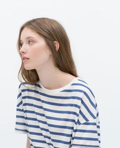 Woman with long hair wearing a blue and white striped shirt against a white background