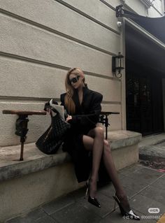 Woman in a black coat and sunglasses sitting outdoors
